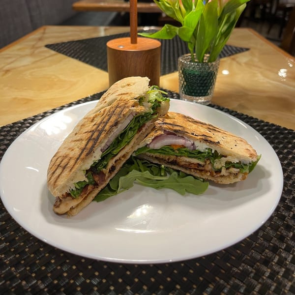 Grilled panini sandwich with chicken, lettuce, and onions on a white plate at Sonia's Gourmet Kitchen.