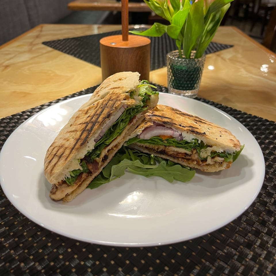 Grilled panini sandwich with chicken, lettuce, and onions on a white plate at Sonia's Gourmet Kitchen.