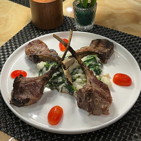 Grilled lamb chops with creamy spinach risotto and cherry tomatoes on a white plate.