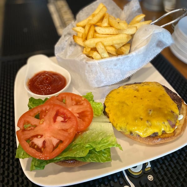 A cheeseburger with lettuce and tomato, a side of fries, and ketchup on a white plate.