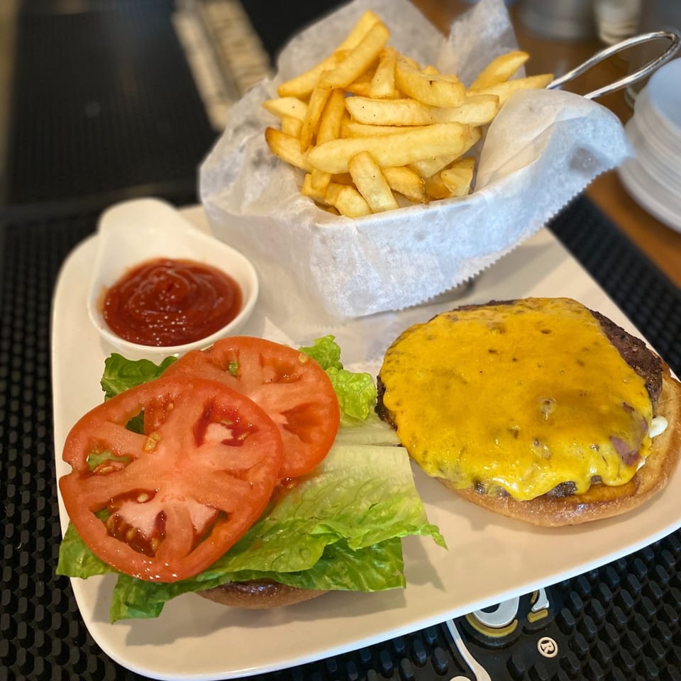 A cheeseburger with lettuce and tomato, a side of fries, and ketchup on a white plate.