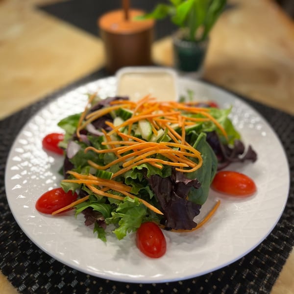 A fresh garden salad with mixed greens, shredded carrots, cucumber, and cherry tomatoes on a white plate.