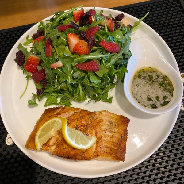 Grilled salmon with lemon slices, a side salad with strawberries and raspberries, and a small dish of sauce.